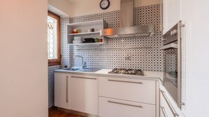 A compact kitchen with white cabinets, a stainless steel sink, a gas stove, and patterned backsplash tiles. - Venezia Terrace (Florence)