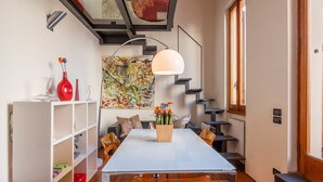 A dining area with a white table, chairs, a vase with flowers, a staircase, and a wall with abstract art. - Venezia Terrace (Florence)