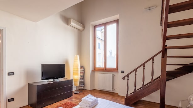 A bedroom with a bed, a TV on a dresser, a window, a radiator, and a wooden staircase. - Venezia Terrace (Florence)