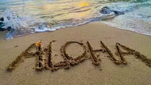 A beach with waves, a sunset, and the word 'ALOHA' written in the sand. - Cozy 1-bedroom condo at Turtle Bay, North Shore AC, private lanai, full kitchen. (Kahuku)