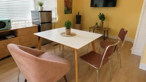 Una cucina moderna con zona pranzo, caratterizzata da un tavolo bianco, sedie rosa e una TV a schermo piatto appesa al muro.