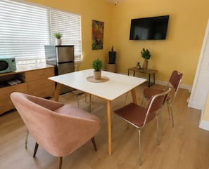 Eine moderne Küche mit Essbereich, mit einem weißen Tisch, rosafarbenen Stühlen und einem Flachbildfernseher an der Wand.