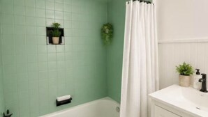 Un bagno con una vasca, un box doccia, un lavabo con dispenser di sapone e una pianta in vaso appesa al muro.