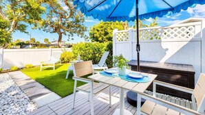 A patio with a table set for two, a blue umbrella, and a white fence. - Lido Bungalow Walk to Beach & St. Armand's Circle (Sarasota)