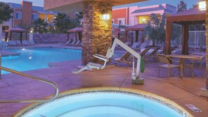Zwembadgedeelte met ligbedden, een jacuzzi en een stenen pilaar.