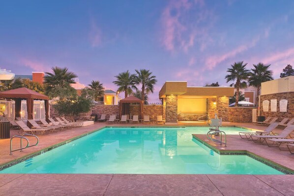 A pool area with lounge chairs, a small gazebo, and a stone wall.