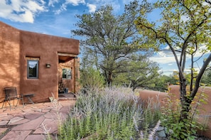 A rustic building with a stone patio, outdoor seating, and a garden with various plants.