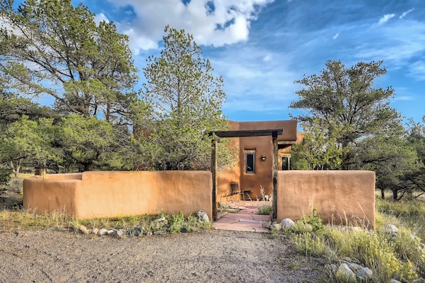 A rustic building with a covered entrance, surrounded by natural vegetation and a clear sky.