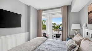Ein Hotelzimmer mit Bett, Fernseher, Balkon mit Sitzgelegenheiten und einer Lampe.