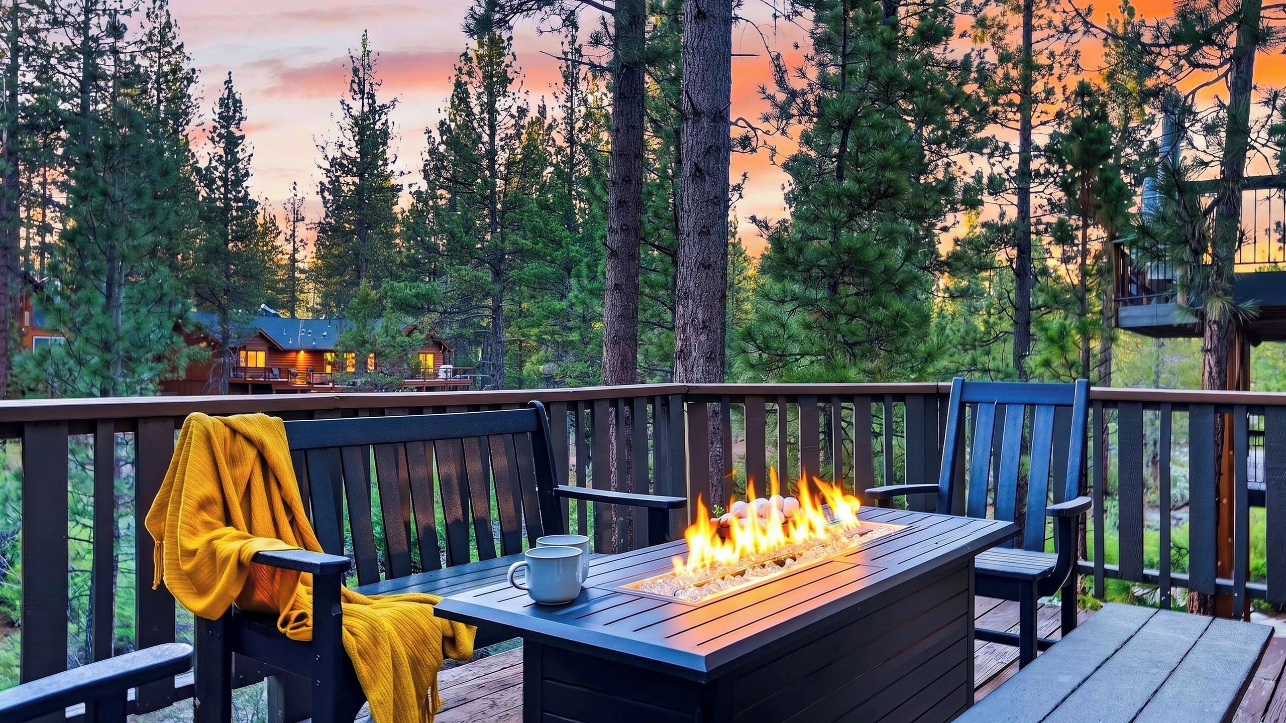 Eine Terrasse mit Feuerstelle, Sitzgelegenheiten und Blick auf eine bewaldete Landschaft.