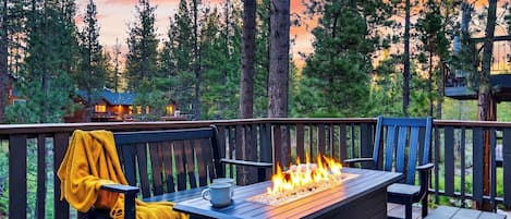 Una terraza con una chimenea, asientos y vistas a un área boscosa.