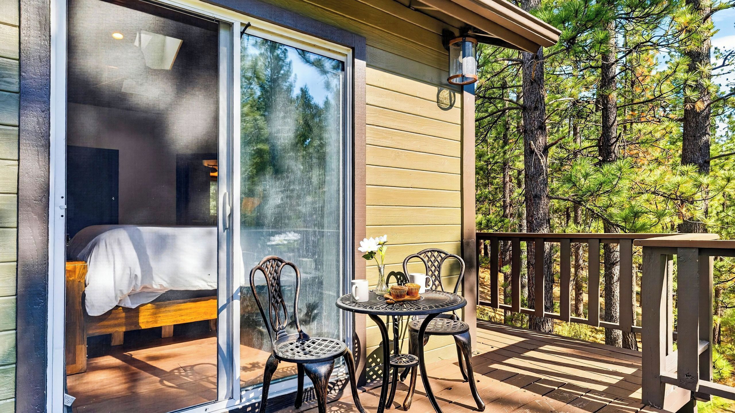 Une pièce dotée d’une porte-fenêtre coulissante, d’un lit, d’une petite table avec des chaises et offrant une vue sur les arbres.