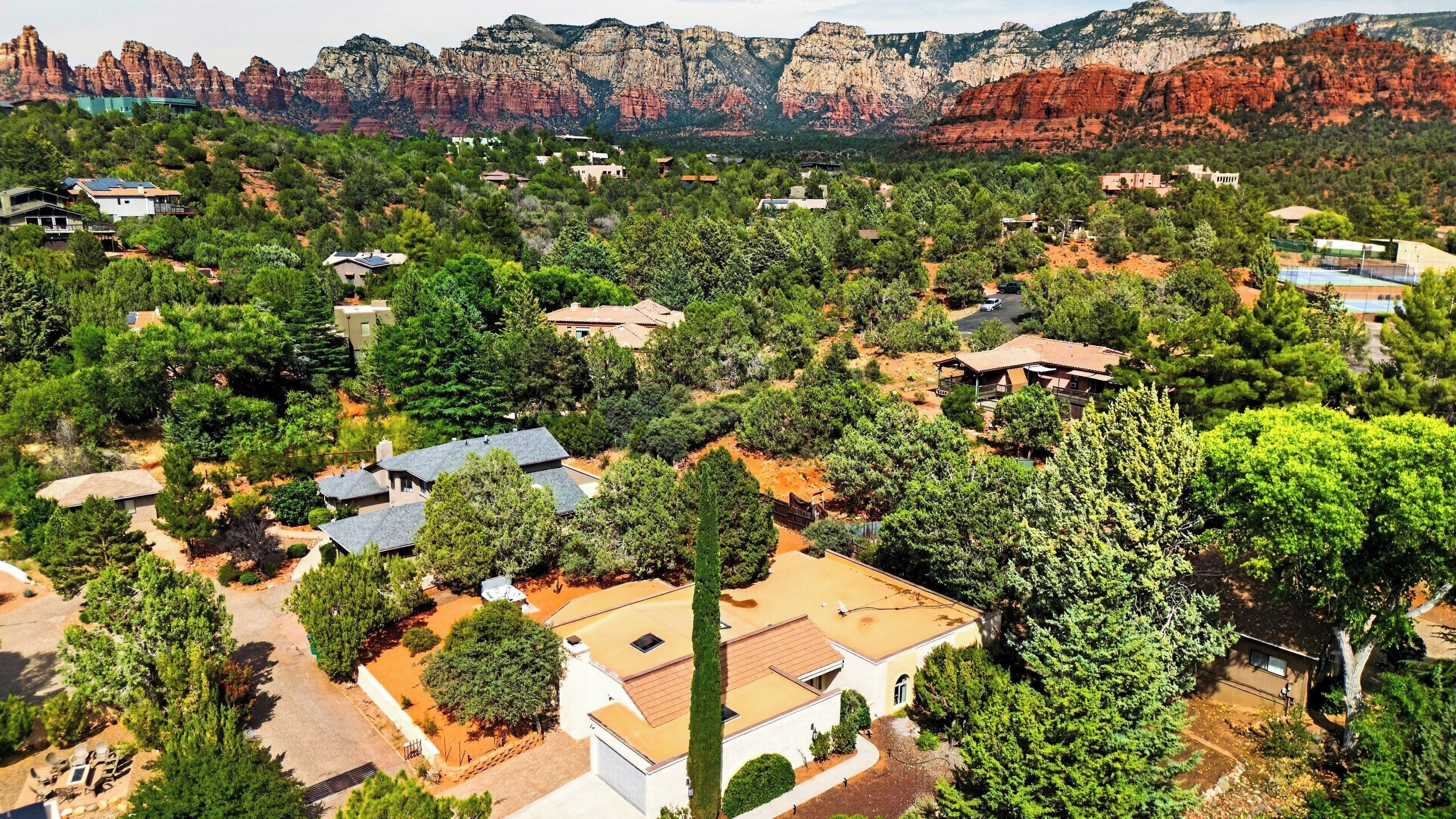 A residential area with houses surrounded by trees and red rock formations in the background.