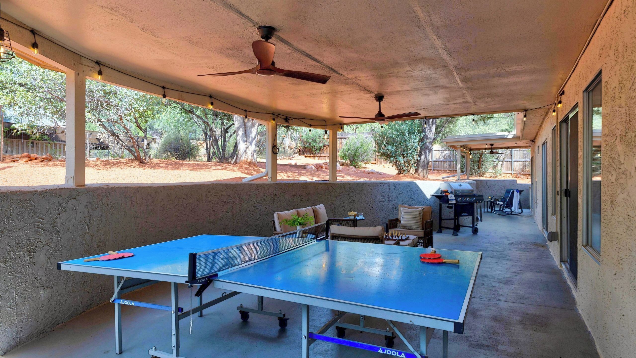 An outdoor covered patio with a ping pong table, seating, and a grill area.