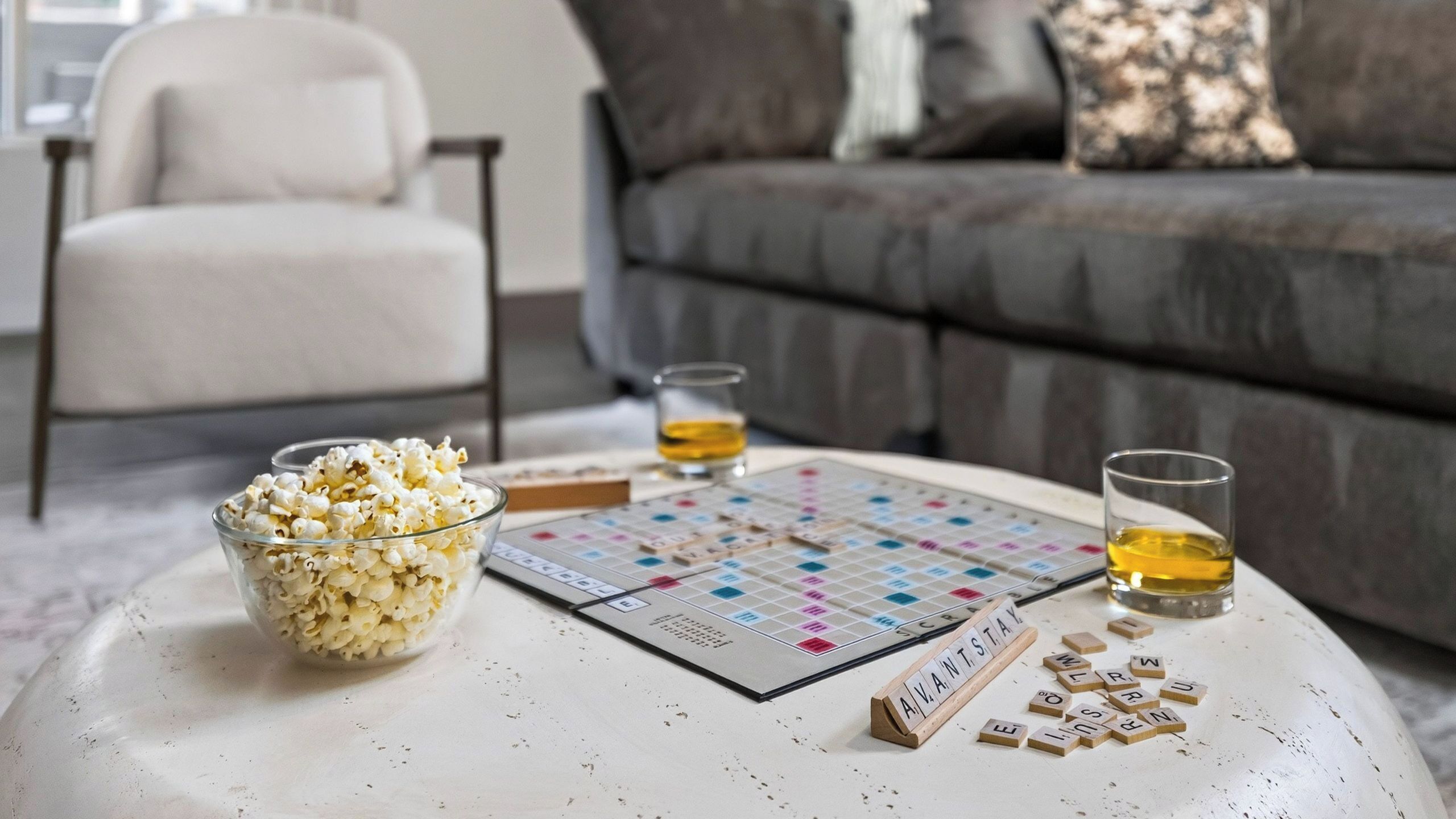 A board game, a bowl of popcorn, and two glasses of amber liquid on a round table.