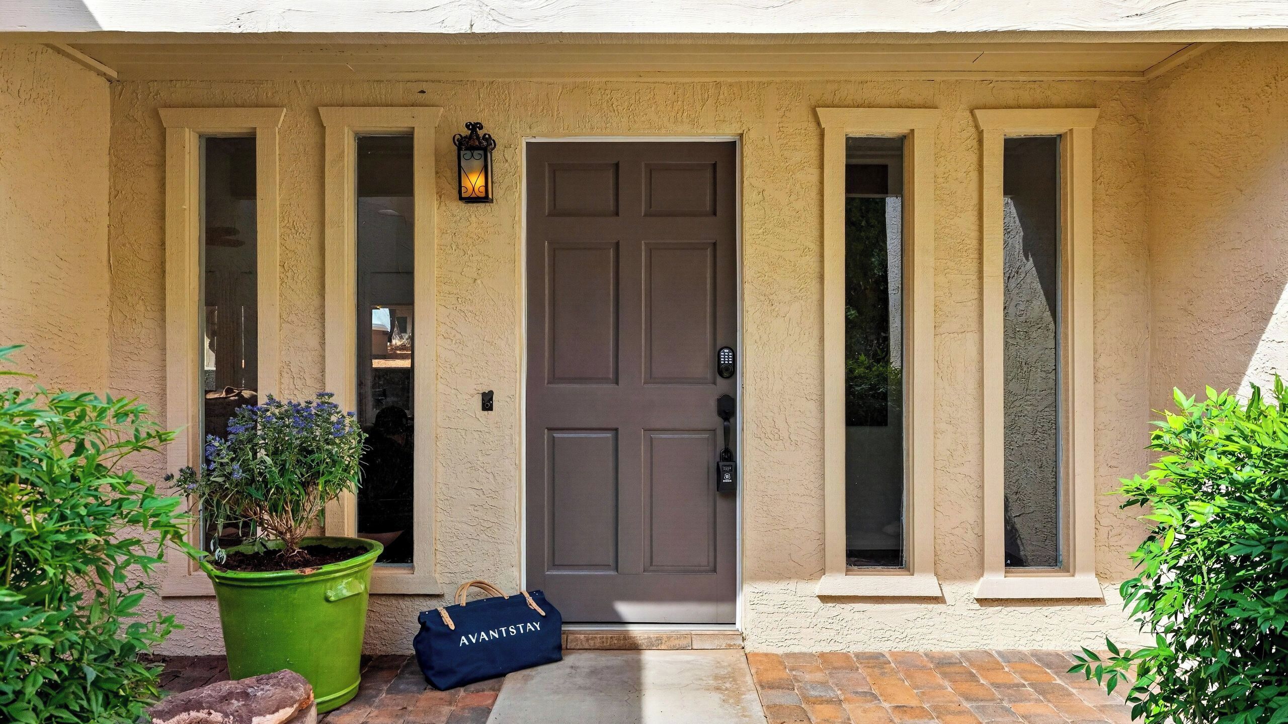 A beige building with a brown door, a green planter, and a blue bag labeled 'AVANTSTAY' on the ground.