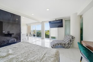 Ein modernes Schlafzimmer mit einem großen Bett, einem an der Wand montierten Fernseher und einem Balkon mit Blick.