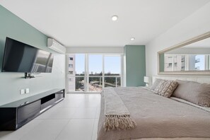 Ein modernes Schlafzimmer mit einem großen Bett, einem Flachbildfernseher, einem Balkon mit Aussicht und einem großen Spiegel.