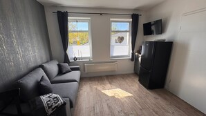 Uma sala de estar moderna com um sofá cinzento, um armário preto, uma TV de tela plana e uma janela com cortinas.
