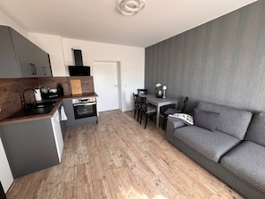 Une cuisine moderne dotée d’un four encastré, un coin repas avec une table et des chaises, et un canapé gris.