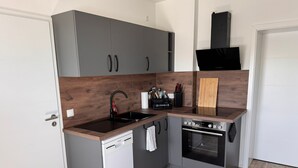 Uma cozinha compacta com armários cinza, uma máquina de lavar louça, um fogão e bancada de madeira.