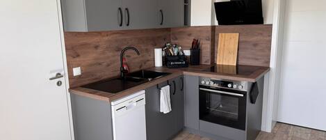 A compact kitchen with grey cabinets, a dishwasher, a stove, and a wooden countertop.