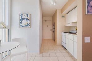 A modern kitchen with white cabinets, a stove, and a dining area with a table and chairs. - ESJ Towers Studio- Beach Access (isla verde)
