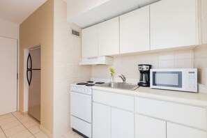 A compact kitchen with white cabinets, a stove, a microwave, and a coffee maker. - ESJ Towers Studio- Beach Access (isla verde)