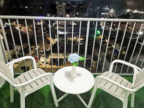 A balcony with two white chairs and a small round table, featuring a vase with a blue flower. - ESJ Towers Studio Isla Verde with Queen Beds (isla verde)