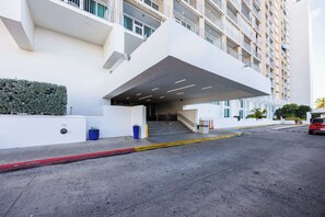 A modern building with a covered entrance, a staircase leading to an upper level, and a parking area with a red curb. - ESJ Towers Studio- Beach Access (isla verde)