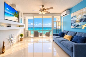A modern living room with a blue couch, a television, and a view of the ocean through large glass doors. - 1BR Beachfront Apt with Queen Bed Isla Verde (aven ida)
