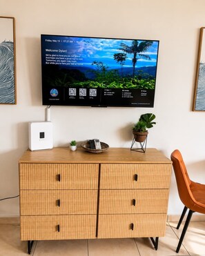 Ein modernes Zimmer mit Fernseher, Holzschrank mit Schubladen, einer kleinen Pflanze und einem Sessel.