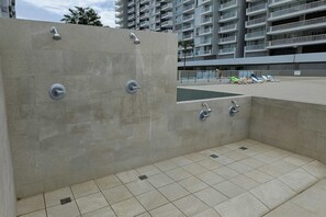 Ein moderner Außenbereich mit Dusche, mehreren Brausen, Fliesenboden und einem Pool im Hintergrund.