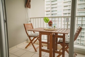 Ein Balkon mit Holztisch und -stühlen, einem Blumentopf und Blick auf ein Hochhaus.