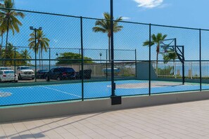 Ein Basketballplatz mit einem Drahtzaun, Palmen und geparkten Autos im Hintergrund.