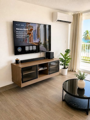 Ein modernes Wohnzimmer mit einem an der Wand befestigten Flachbildfernseher, einer Holzunterhaltungseinrichtung darunter, einem runden schwarzen Couchtisch und einer Kühlpflanze.