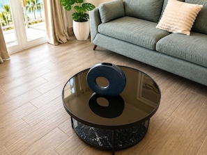 Uma sala de estar moderna com uma mesa de centro redonda de vidro, um sofá cinza e um vaso de planta.