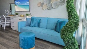 Ein Wohnzimmer mit blauem Sofa, einem runden Hocker, einem Schreibtisch mit Stuhl und einer Wand mit Dekotellern.