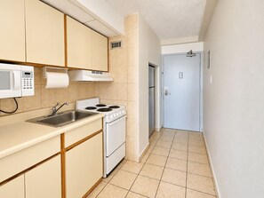 A compact kitchen with a microwave, stove, sink, and a door leading to another room. - Isla Verde ESJ Towers Studio Apt with Queen Beds (Avenida Isla)