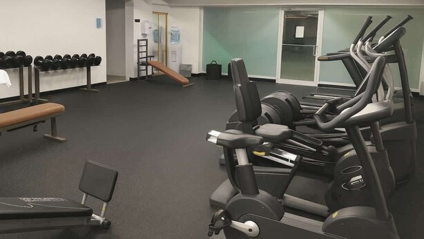 Ein Fitnessraum mit Trainingsgeräten, einer Bank und einem Wasserspender.