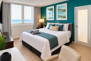 Een hotelkamer met een bed, een bureau, een stoel, een lamp en uitzicht op de zee.