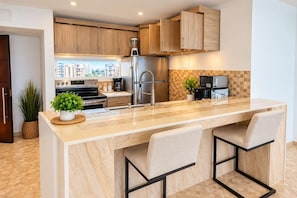 A modern kitchen with a central island, stainless steel appliances, and wooden cabinetry. - Queen Bed in 1BR Beachfront Apt Condado San Juan (SanJuan)