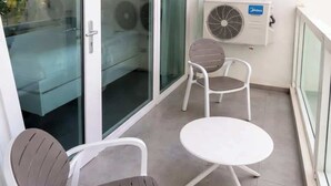 A balcony with two chairs and a small table, a glass door, and an air conditioning unit. - ESJ Towers Studio - Walk to the Beach (Avenida Isla)