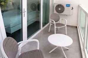 Ein Balkon mit zwei Stühlen, einem kleinen Tisch, einer Glastür und einer Klimaanlage.