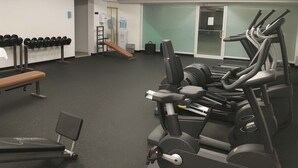 Un gimnasio con equipo de ejercicio, una banca y un soporte para mancuernas en la pared.
