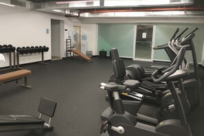 Ein Fitnessraum mit Trainingsgeräten, einer Bank und einem an der Wand befestigten Hantelständer.