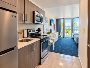 Eine moderne Küche mit Mikrowelle, Herd und Kaffeemaschine. Ein Essbereich mit Tisch und Stühlen ist vorhanden. Das Zimmer verfügt über ein großes Fenster mit Blick auf Palmen.