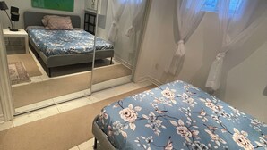 Une chambre à coucher comprenant un lit, une table de chevet, un miroir, une fenêtre avec des rideaux et une œuvre d’art murale de couleur verte.