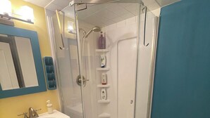 Une salle de bain d’angle avec une douche en verre, un lavabo avec un miroir et des meubles bleus.