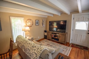 A living room with a sofa, a television, a lamp, and a door. - Unique log cabin in West Jefferson! PRIVATE/HOT TUB/The Bird's Nest (West Jefferson)